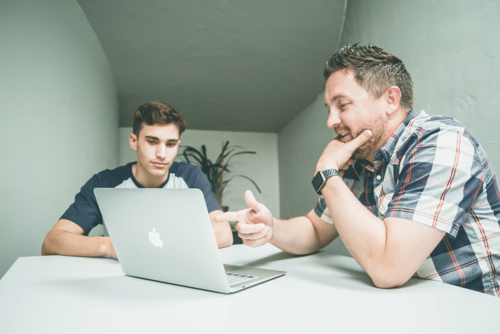 image of a man wearing a plaid shirt pointing at the silver MacBook